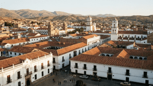 Fotografía panorámica realista de la Ciudad Blanca de Sucre, Chuquisaca, destacando la arquitectura colonial neoclásica y los techos de teja roja al atardecer